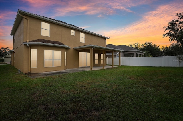 back house at dusk featuring a yard and a patio