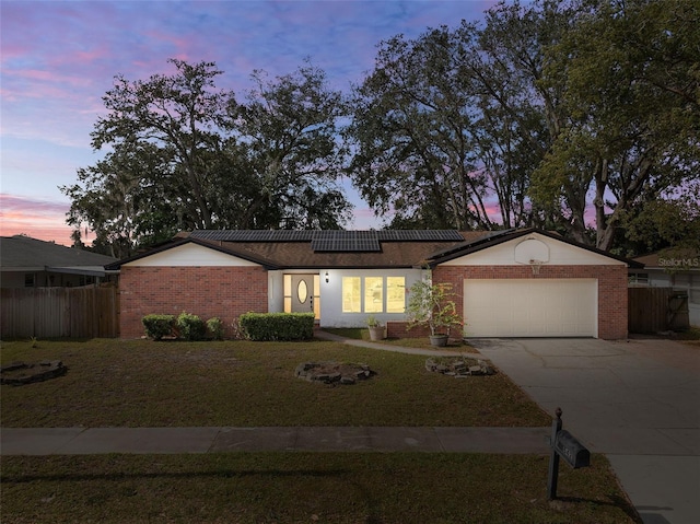 ranch-style house with solar panels, concrete driveway, a lawn, an attached garage, and fence