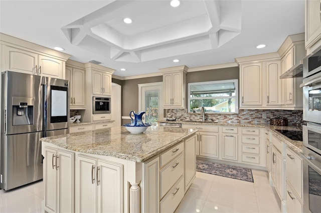 kitchen featuring light stone counters, a center island, decorative backsplash, cream cabinets, and appliances with stainless steel finishes