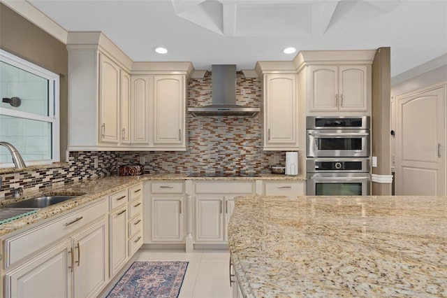 kitchen with tasteful backsplash, recessed lighting, a sink, light stone countertops, and wall chimney exhaust hood