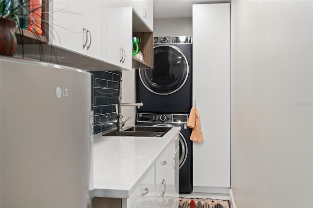 laundry area featuring stacked washer / drying machine, cabinet space, and a sink