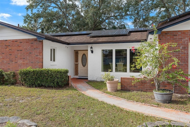 view of front of house featuring brick siding, a front yard, roof mounted solar panels, and stucco siding