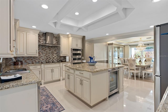 kitchen with decorative backsplash, appliances with stainless steel finishes, a sink, wall chimney range hood, and beverage cooler