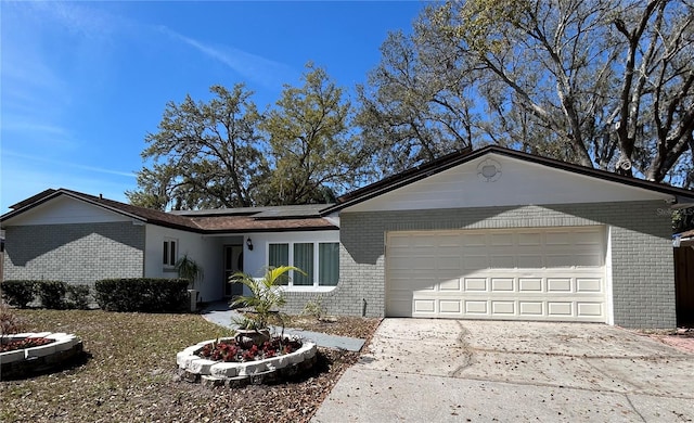 ranch-style home featuring driveway, brick siding, an attached garage, and roof mounted solar panels