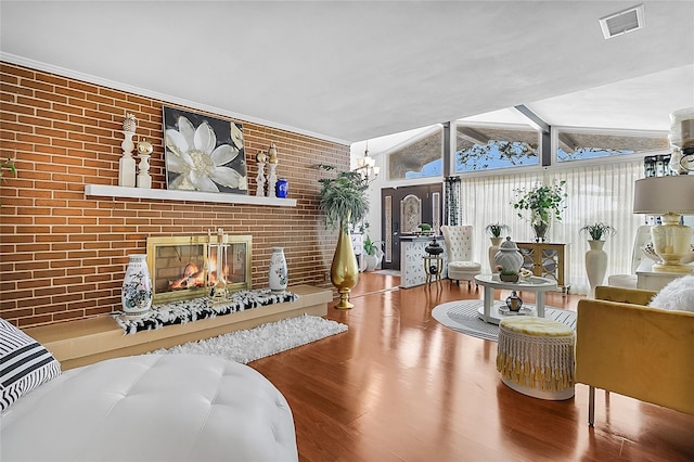 living room with a fireplace, brick wall, hardwood / wood-style flooring, and vaulted ceiling