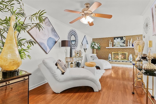 living area featuring a fireplace, wood finished floors, a ceiling fan, baseboards, and crown molding