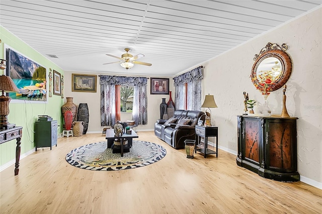 sitting room featuring a textured wall, ceiling fan, baseboards, and wood finished floors