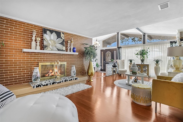 living area with lofted ceiling, visible vents, a brick fireplace, brick wall, and wood finished floors