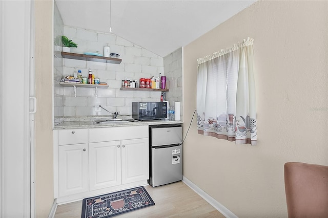 kitchen featuring open shelves, light countertops, decorative backsplash, freestanding refrigerator, and a sink