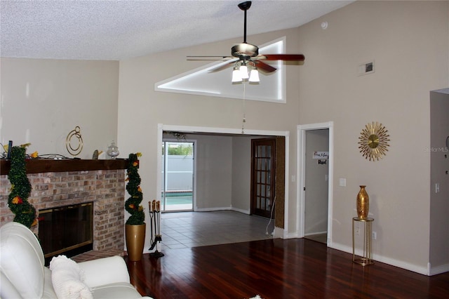 living room featuring a textured ceiling, dark hardwood / wood-style flooring, high vaulted ceiling, a brick fireplace, and ceiling fan