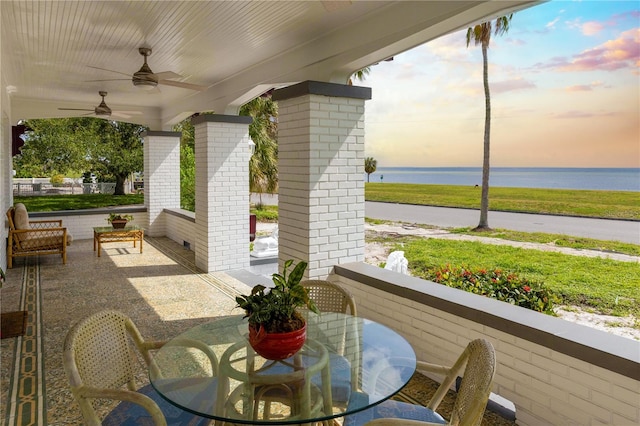 patio terrace at dusk featuring ceiling fan and a water view