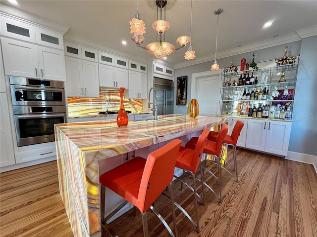 kitchen with white cabinetry, appliances with stainless steel finishes, a kitchen breakfast bar, decorative light fixtures, and an island with sink