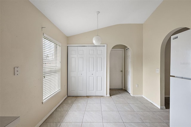 unfurnished bedroom featuring light tile patterned flooring, a closet, white refrigerator, and vaulted ceiling