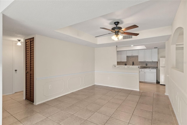 kitchen featuring white cabinetry, white refrigerator, decorative backsplash, kitchen peninsula, and ceiling fan