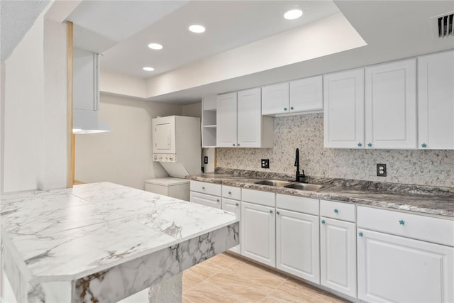 kitchen featuring white cabinetry, sink, stacked washer / dryer, and tasteful backsplash