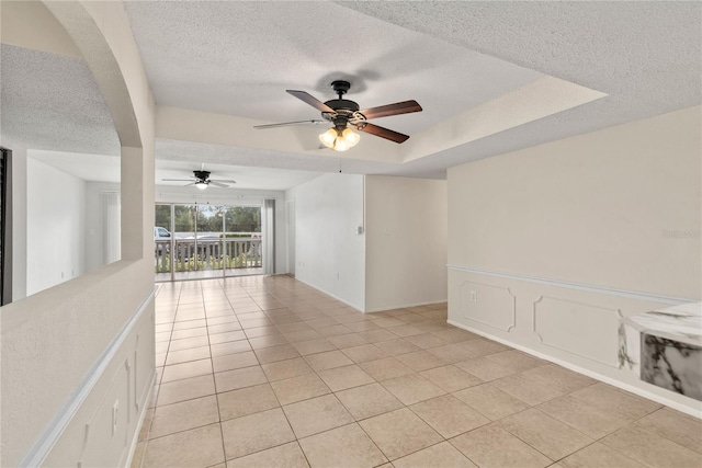 empty room with ceiling fan, a textured ceiling, light tile patterned floors, and a raised ceiling