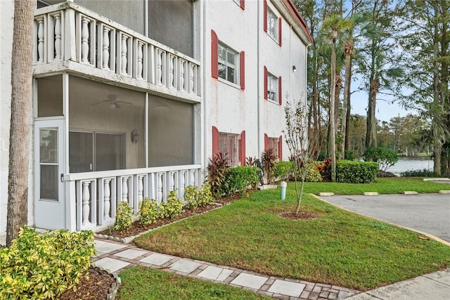 view of side of property featuring ceiling fan, a balcony, and a yard