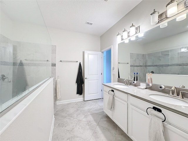 bathroom with tile patterned flooring, vanity, a textured ceiling, and a tile shower