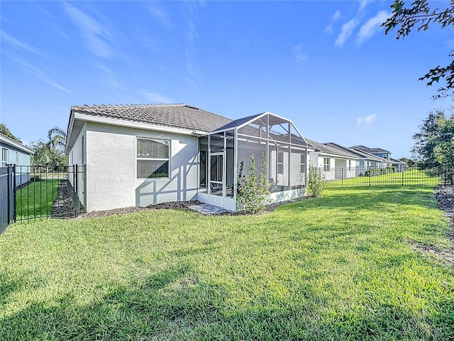 rear view of property with glass enclosure and a lawn