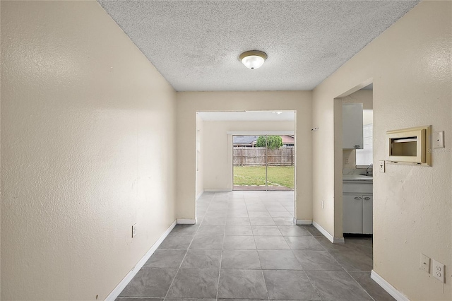 hall featuring a textured ceiling, sink, and light tile patterned floors