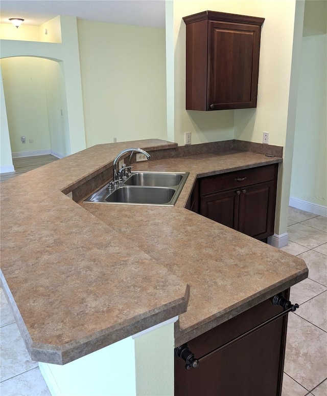 kitchen with sink, dark brown cabinetry, kitchen peninsula, and light tile patterned flooring