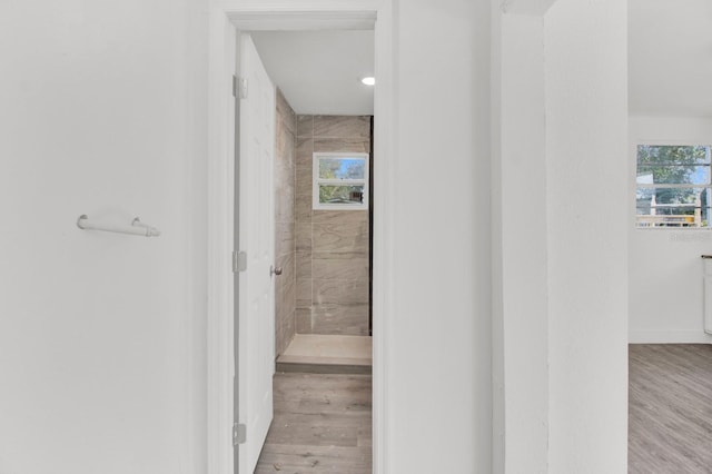 bathroom with a wealth of natural light, wood-type flooring, and tiled shower