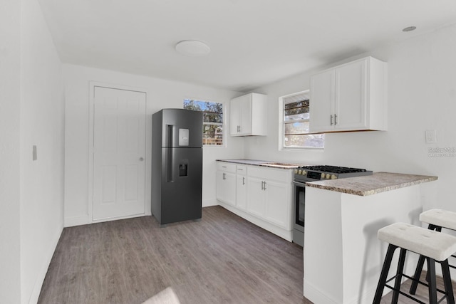 kitchen with black refrigerator, a kitchen bar, light wood-type flooring, stainless steel gas range oven, and white cabinetry