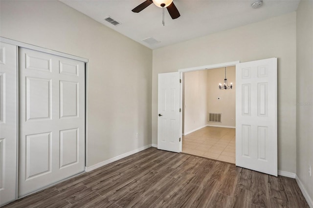 unfurnished bedroom with dark hardwood / wood-style flooring, a closet, and ceiling fan with notable chandelier