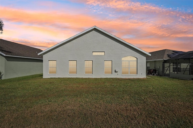 back house at dusk with a lanai and a yard