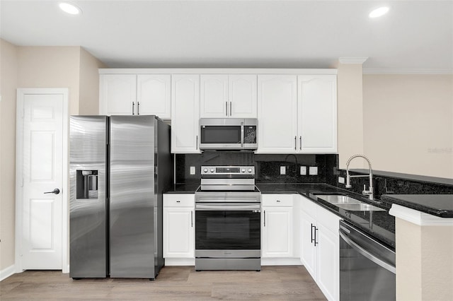 kitchen with stainless steel appliances, white cabinetry, sink, dark stone countertops, and light hardwood / wood-style flooring