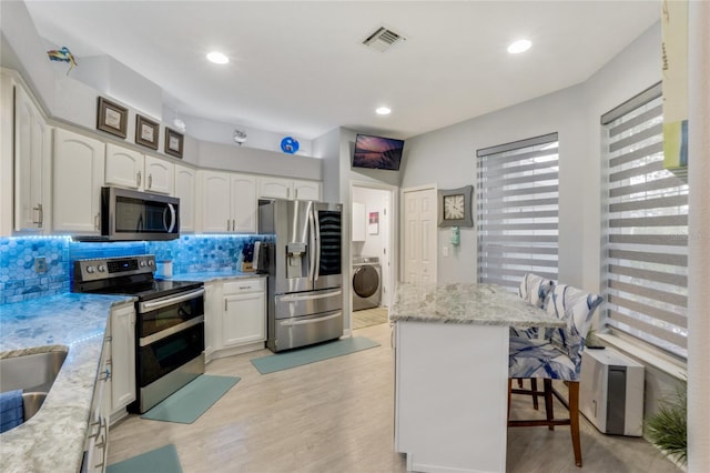 kitchen featuring white cabinets, a breakfast bar area, light wood-type flooring, washer / dryer, and stainless steel appliances