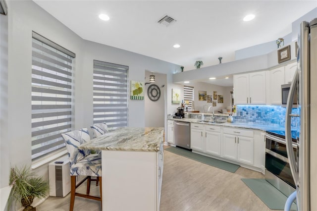 kitchen with a kitchen breakfast bar, stainless steel appliances, sink, light hardwood / wood-style flooring, and white cabinetry