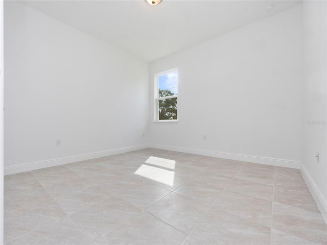 tiled empty room featuring vaulted ceiling