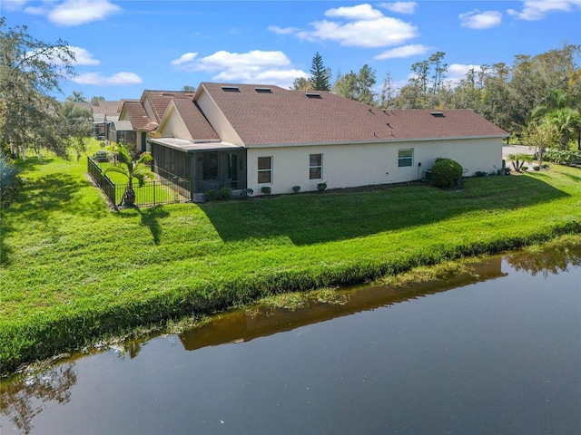 back of property with a water view, a sunroom, and a lawn