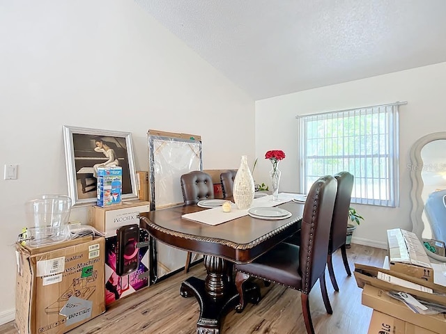 dining area featuring light wood-type flooring, vaulted ceiling, and a textured ceiling