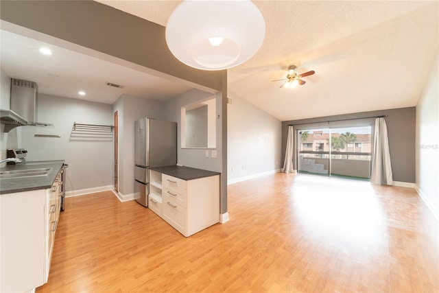 kitchen with white cabinets, light wood-type flooring, wall chimney range hood, and stainless steel fridge