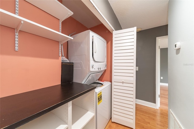 laundry area with stacked washer / drying machine, light wood-type flooring, and a textured ceiling