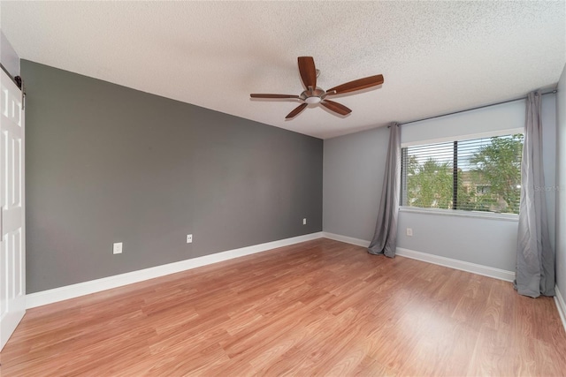 spare room featuring light hardwood / wood-style floors, a barn door, a textured ceiling, and ceiling fan