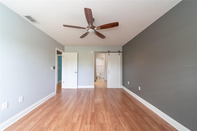 unfurnished bedroom with a textured ceiling, light wood-type flooring, a barn door, and ceiling fan