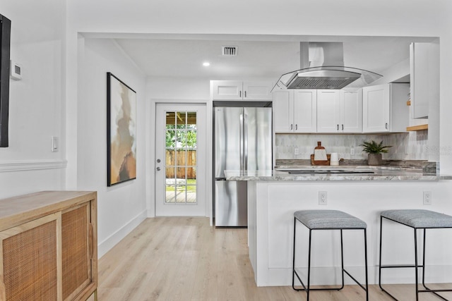 kitchen featuring stainless steel refrigerator, white cabinetry, light stone counters, kitchen peninsula, and island range hood