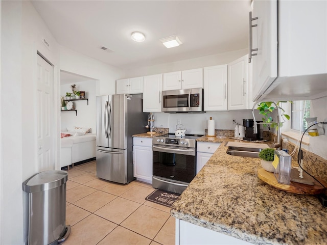 kitchen with white cabinets, appliances with stainless steel finishes, light tile patterned floors, and light stone counters