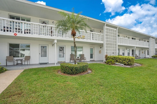 rear view of property featuring a patio, a yard, and a balcony