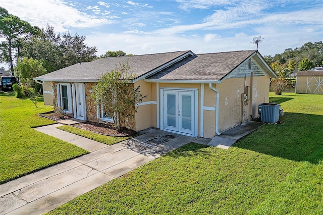 ranch-style house with french doors, an outdoor structure, a front yard, and central AC