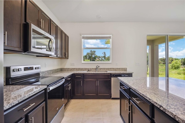 kitchen featuring stainless steel appliances, light stone countertops, sink, and dark brown cabinetry