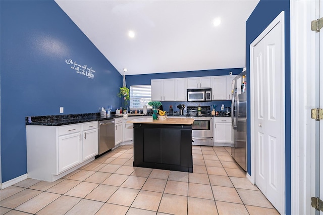 kitchen featuring stainless steel appliances, dark stone counters, a center island, light tile patterned floors, and white cabinetry