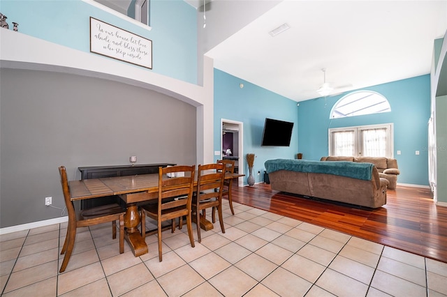 dining room featuring ceiling fan, light hardwood / wood-style floors, and a towering ceiling