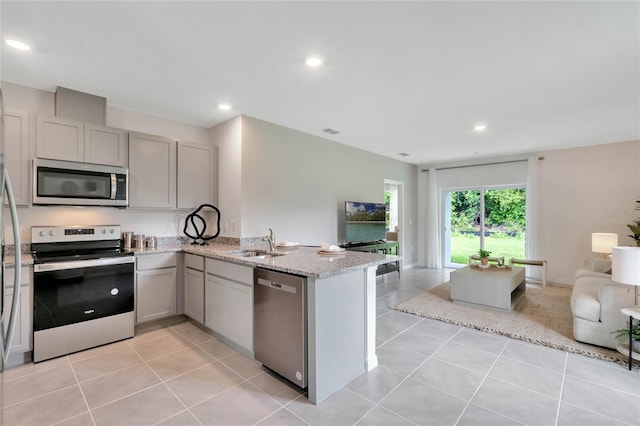 kitchen with light stone counters, appliances with stainless steel finishes, light tile patterned floors, sink, and kitchen peninsula