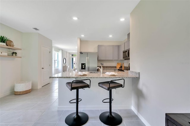 kitchen featuring kitchen peninsula, appliances with stainless steel finishes, a kitchen breakfast bar, light tile patterned floors, and gray cabinets