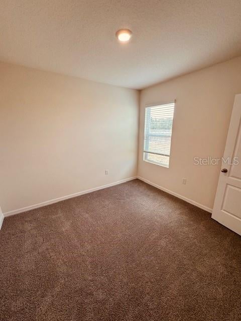 unfurnished room with dark colored carpet and baseboards