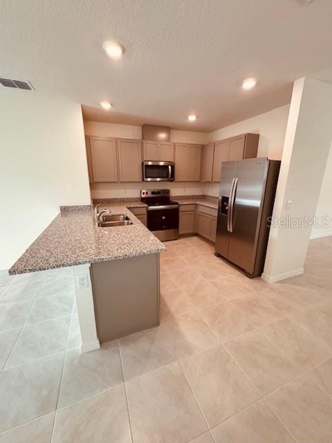 kitchen with visible vents, appliances with stainless steel finishes, light stone counters, a peninsula, and a sink